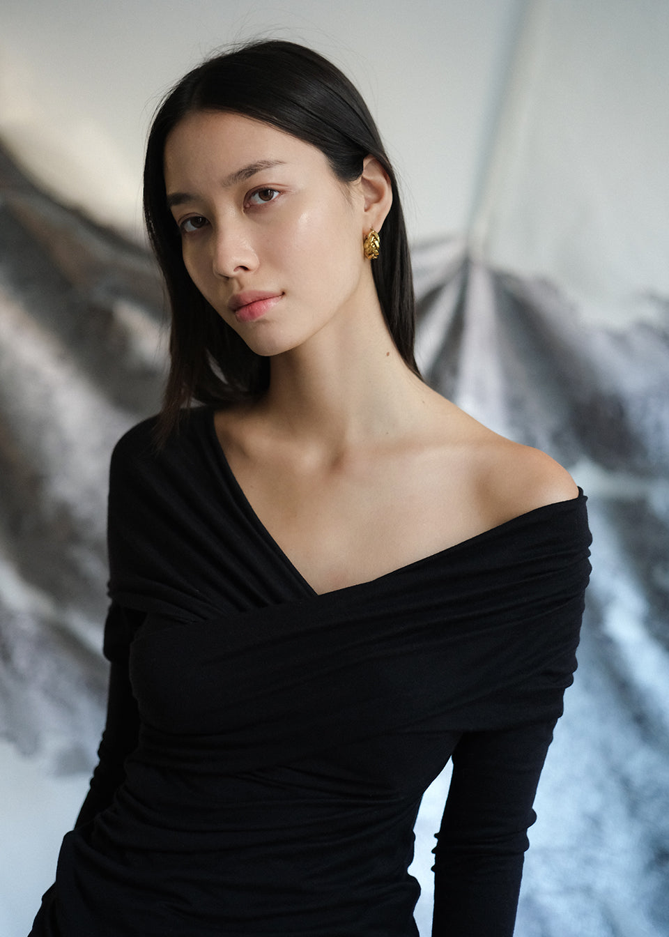 Woman wearing an off-shoulder black top against a textured white background