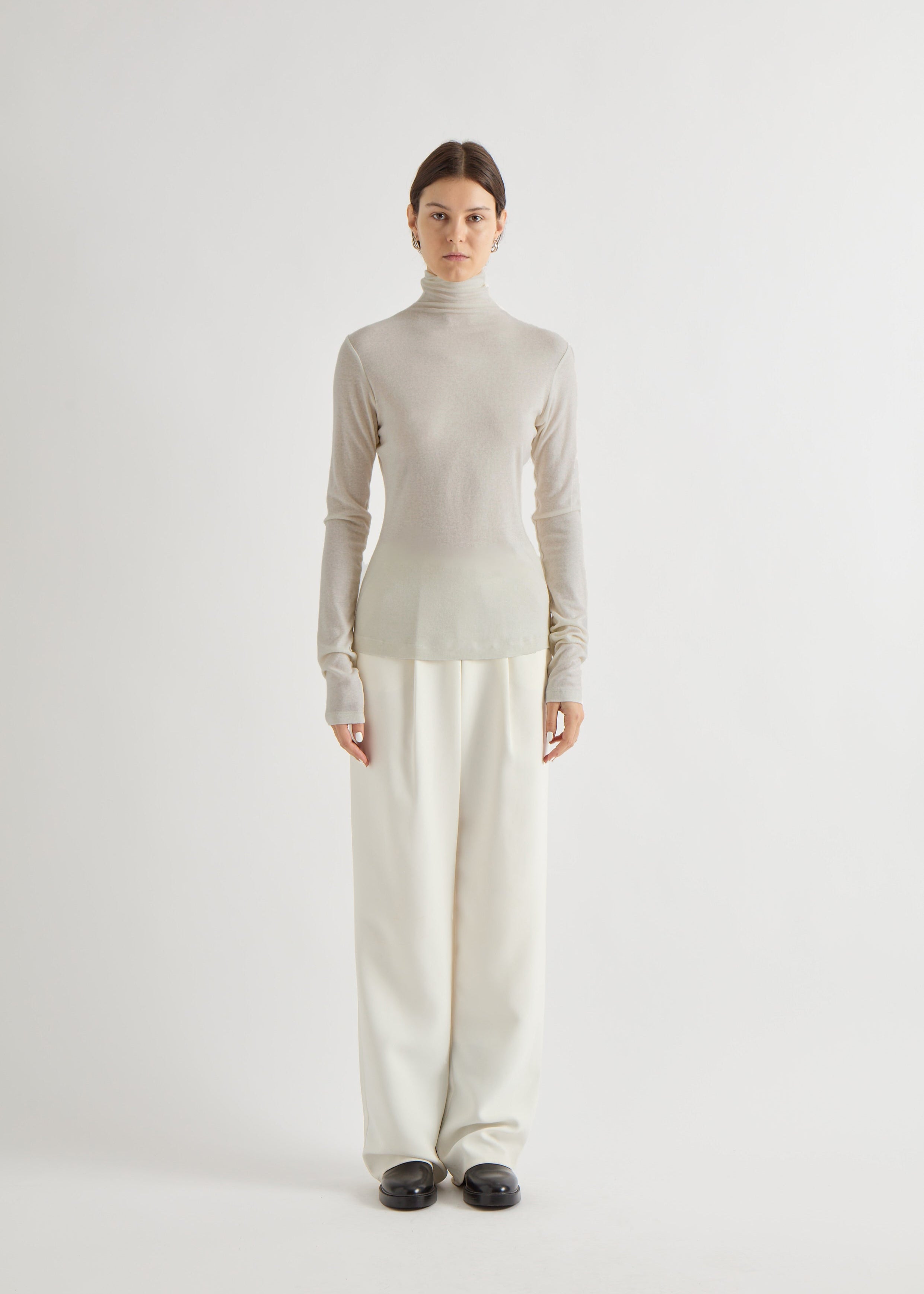 Person wearing a light gray turtleneck sweater and beige pants on a white background.