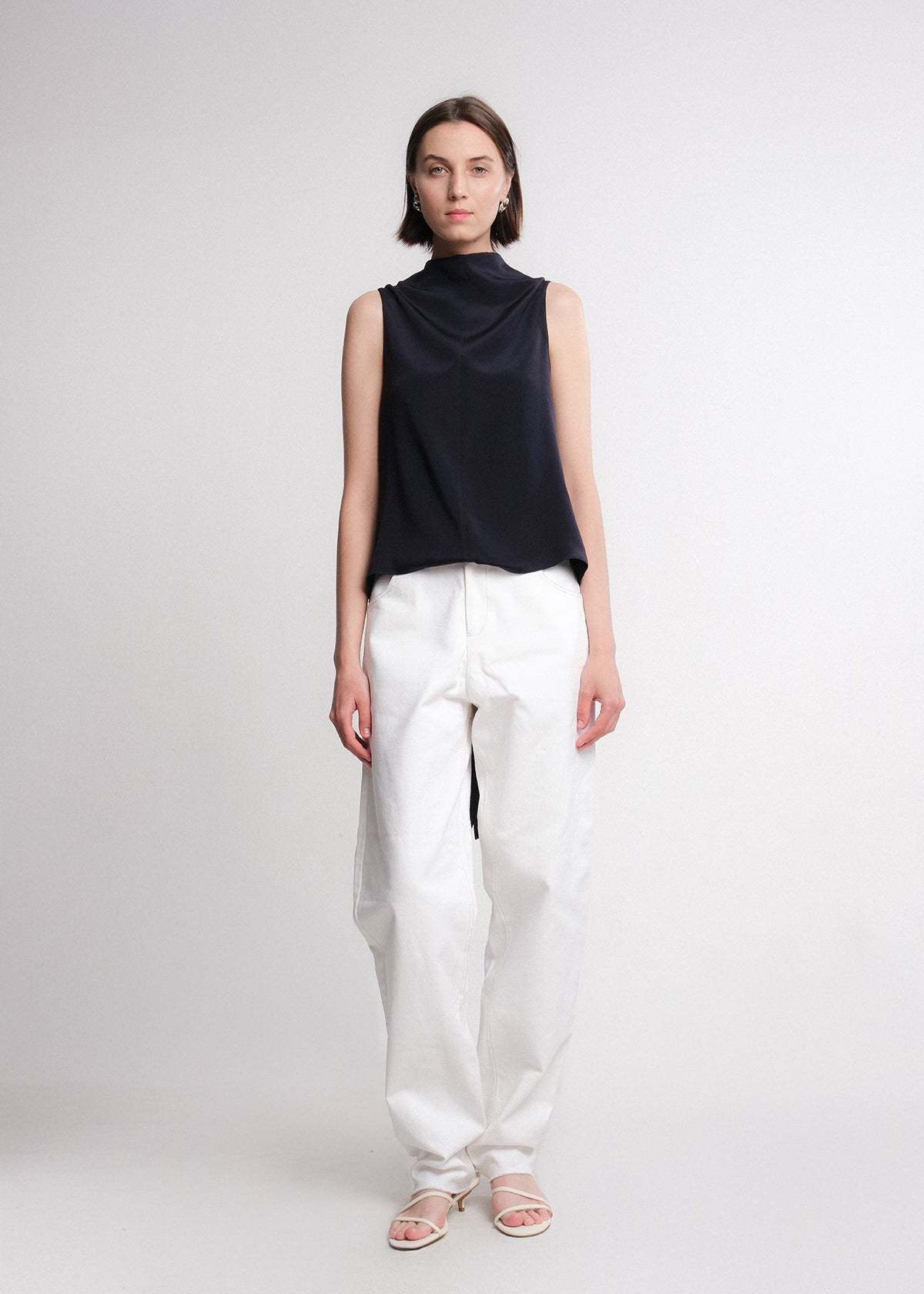 Sleeveless navy silk top with an asymmetrical high-low hem and extended draped back panel tied at the side, featuring a clean crew neckline and soft, fluid silhouette.