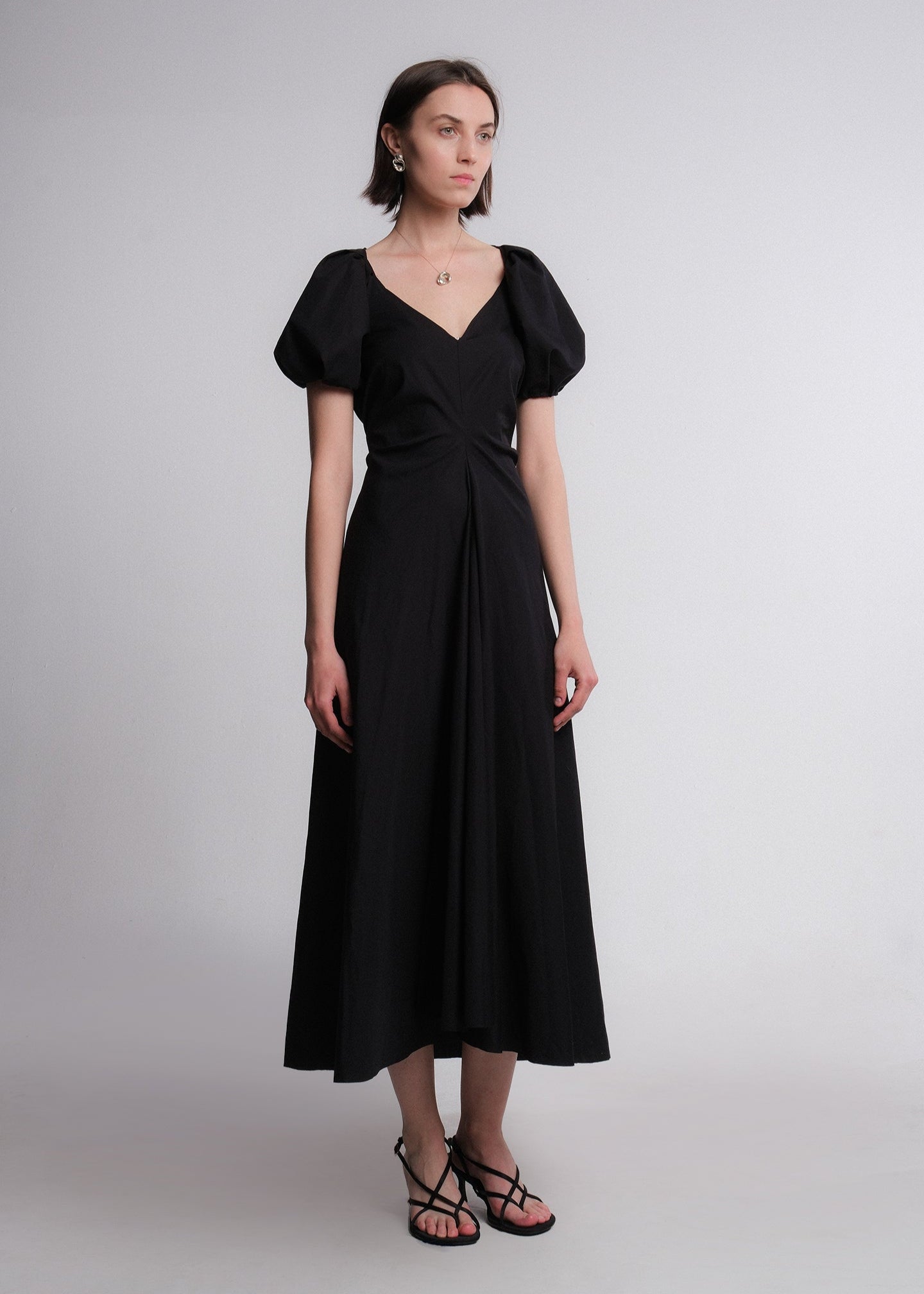 Black maxi dress made of cotton poplin fabric, featuring voluminous puff sleeves, a deep V-neckline, a gusset for added movement, and a flared A-line skirt.