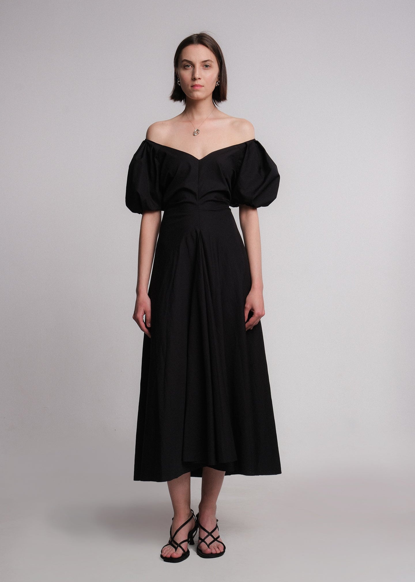 Maxi dress made of black cotton poplin fabric, featuring voluminous puff sleeves, a deep V-neckline, a gusset for added movement, and a flared A-line skirt.