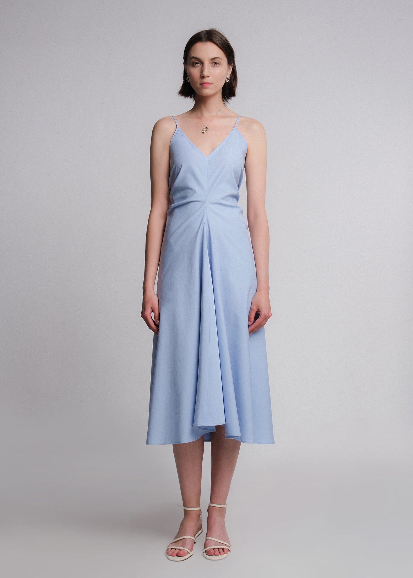 Sleeveless light blue midi dress made from cotton poplin, featuring a deep V-neckline, think spaghetti straps, a structured waist, and a softly flared A-line skirt.