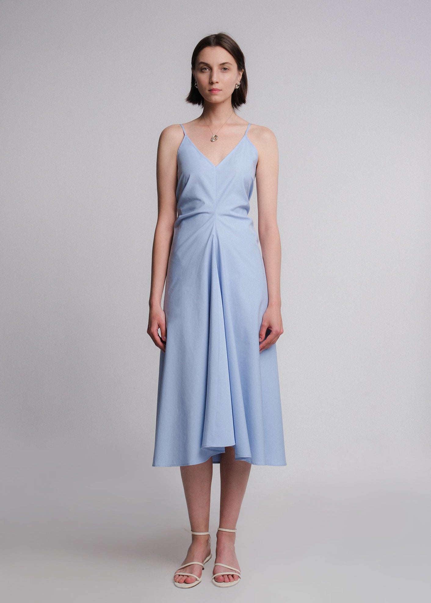 Sleeveless light blue midi dress made from cotton poplin, featuring a deep V-neckline, thin spaghetti straps, a structured waist, and a softly flared A-line skirt.