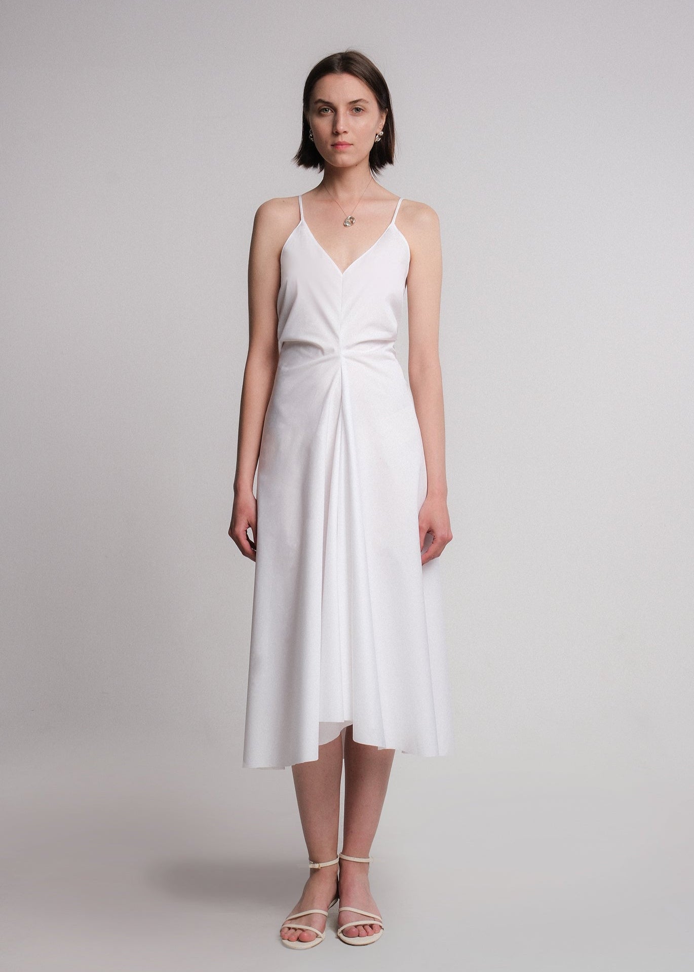 Sleeveless ivory midi dress made from cotton poplin, featuring a deep V-neckline, thin spaghetti straps, a structured waist, and a softly flared A-line skirt.