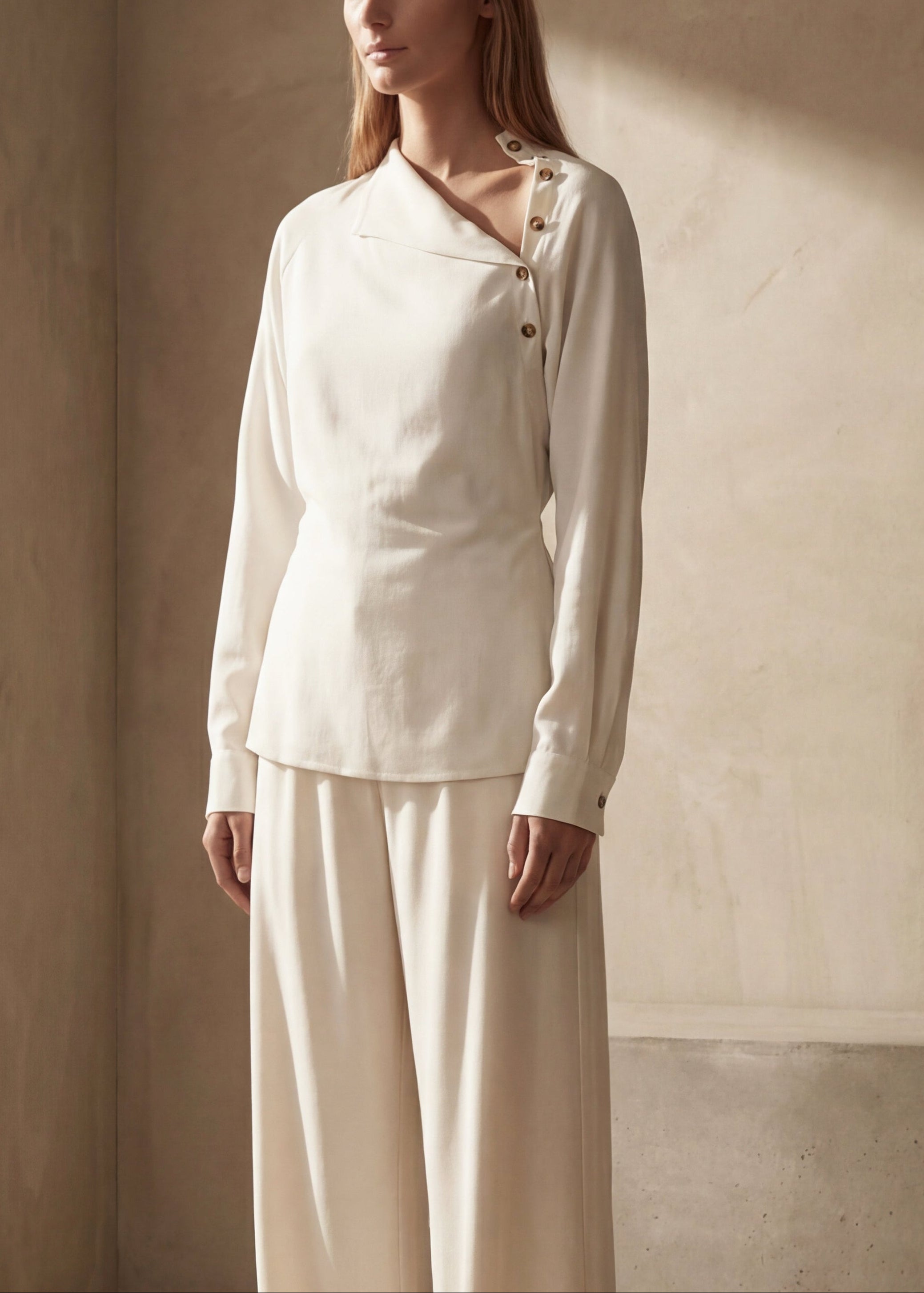 Woman wearing a white long sleeve blouse with side opening detail. 