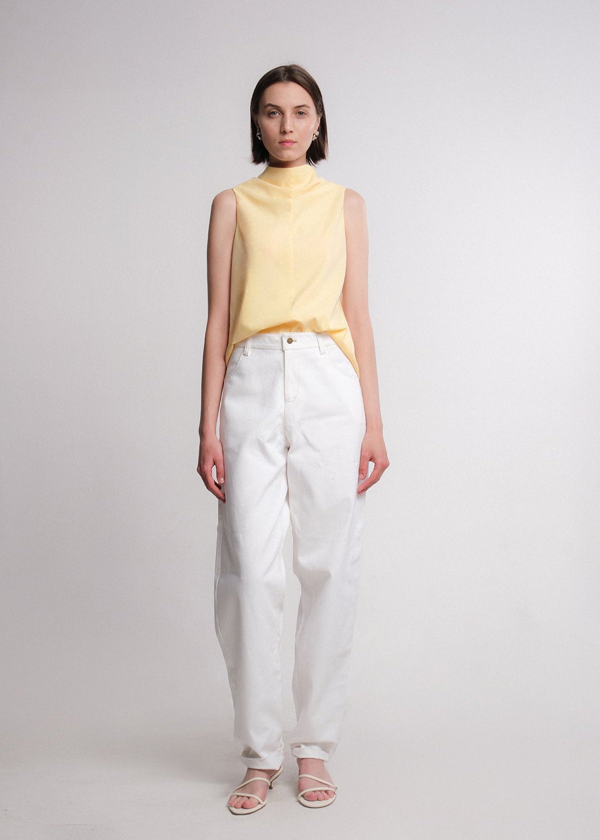 Sleeveless butter yellow cotton-rayon-poly blend top with an asymmetrical high-low hem and extended draped back panel tied at the side, featuring a clean crew neckline and soft, fluid silhouette.