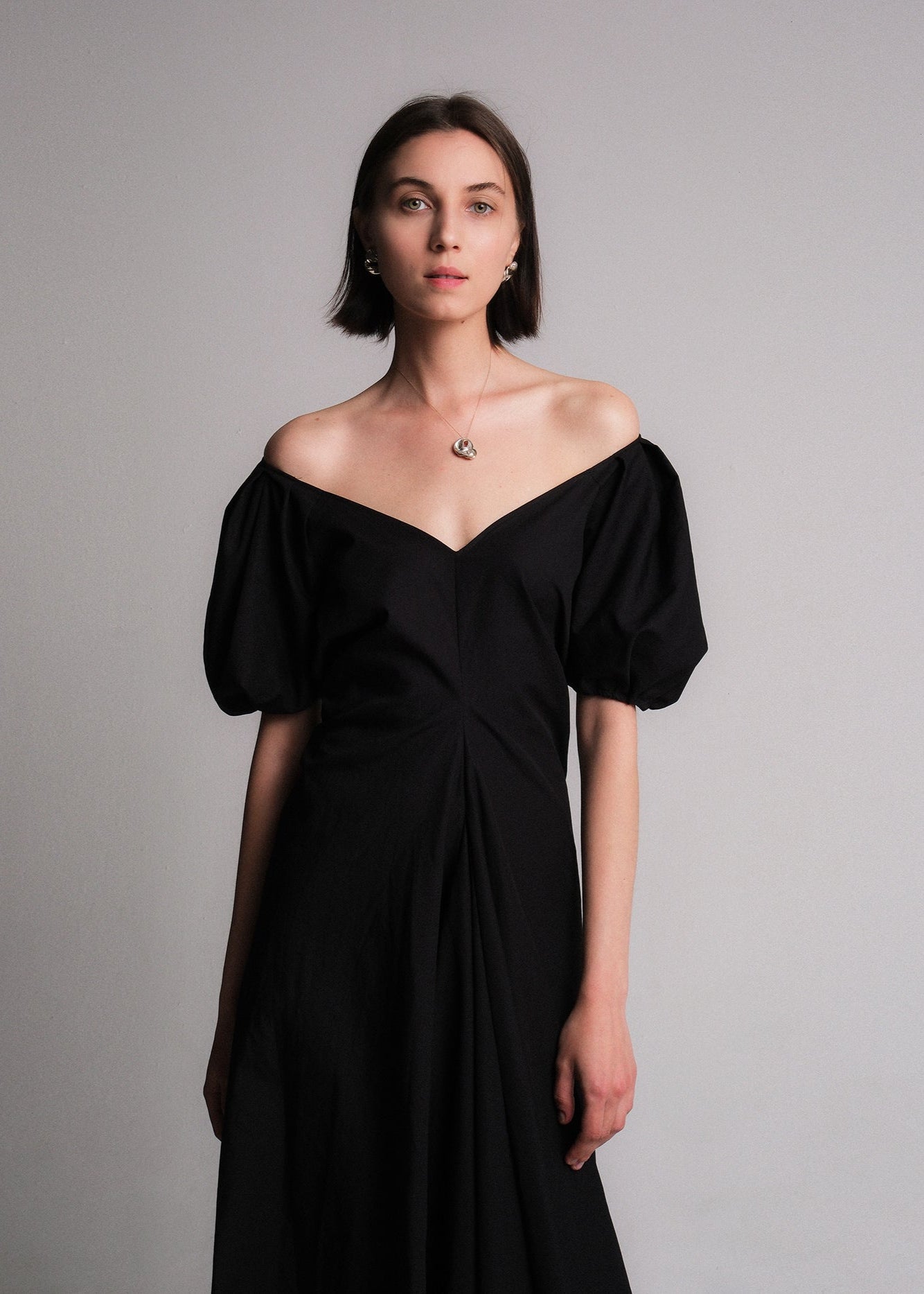 Black maxi dress made of cotton poplin fabric, featuring voluminous puff sleeves, a deep V-neckline, a gusset for added movement, and a flared A-line skirt.